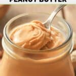 Homemade peanut butter on a spoon over a jar of it.