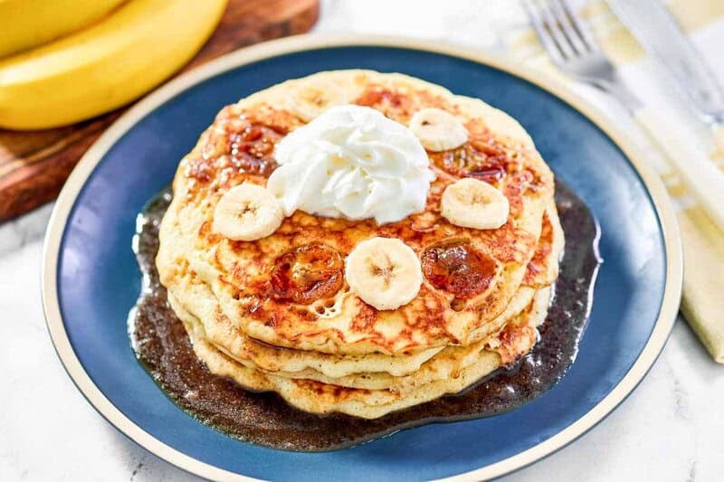 Copycat IHOP bananas foster pancakes with banana slices, brown sugar syrup, and whipped cream.