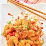 Homemade Panda Express chili crisp shrimp over rice and chopsticks on a plate.