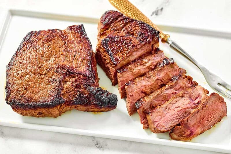 Steaks made with copycat steak and ale kensington club marinade and a meat fork on a platter.