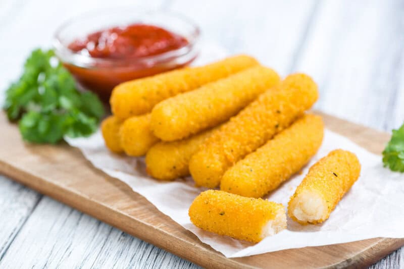 Smoked mozzarella sticks and dipping sauce on a small wood board.